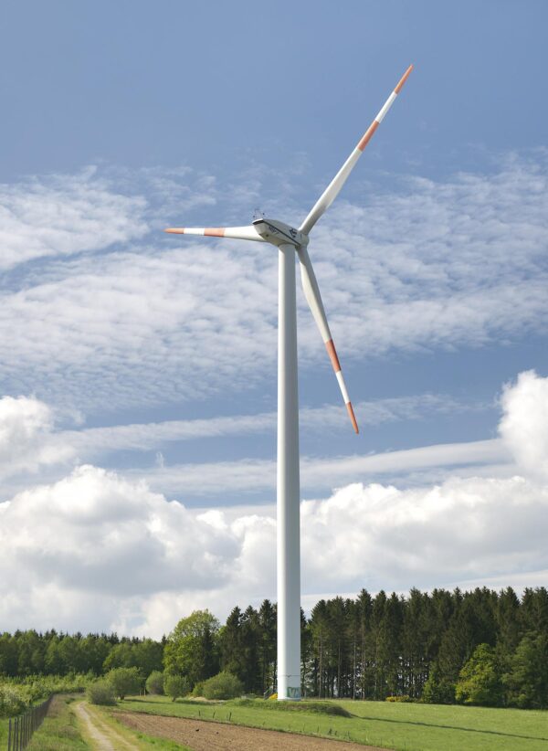 Modern windmill placed on meadow near forest on background of blue sky in countryside